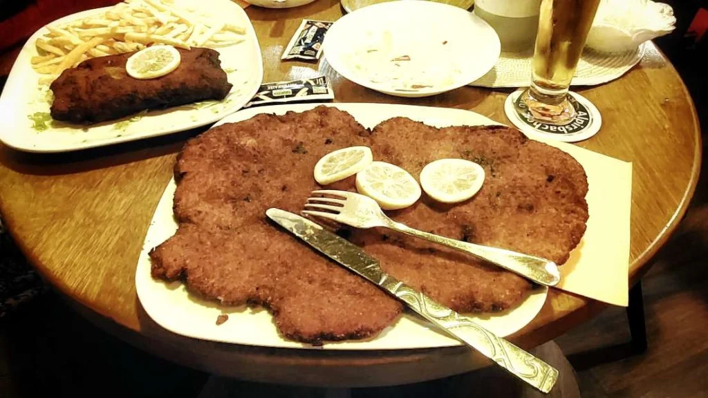 Foto van een XXL Schnitsel, zo groot dat die het hele bord in beslag neemt.